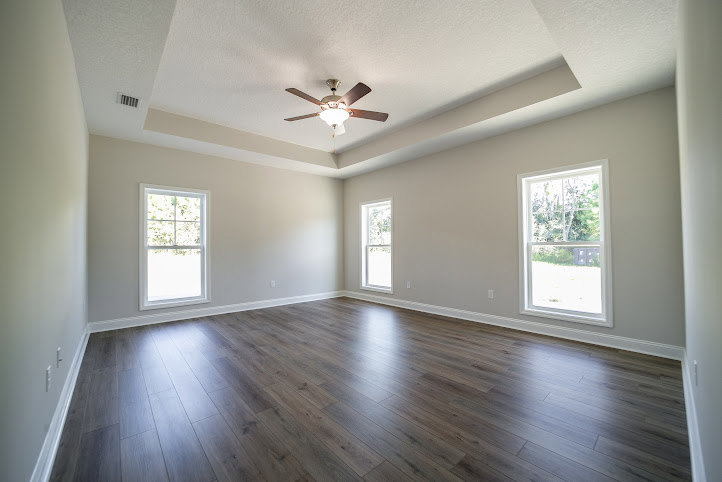 Ceiling fan mounted on white plaster ceiling, large windows with natural light, wood laminate flooring, neutral walls