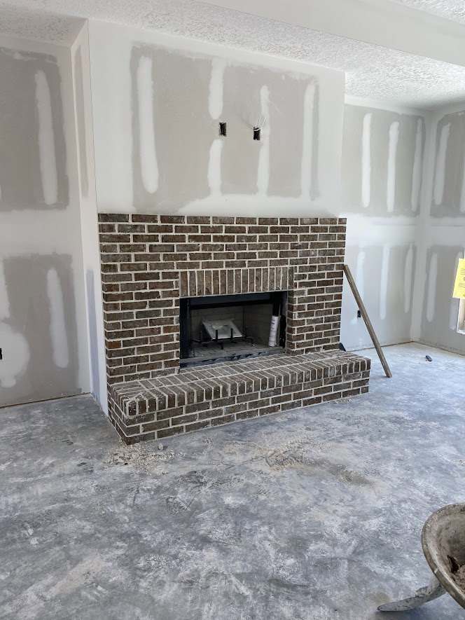 Red brick fireplace with metal fire screen, white painted wall, brick hearth step, wood burning stove, and decorative bowl on shelf