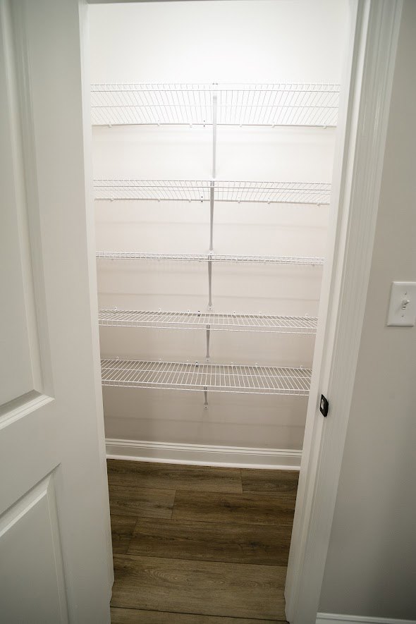 Empty pantry with white wire shelving, wood flooring, and white baseboards