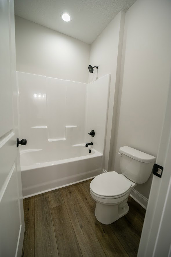 White bathtub and modern toilet in a bathroom with light tile flooring and wall tiles, chrome fixtures, and minimal accessories.