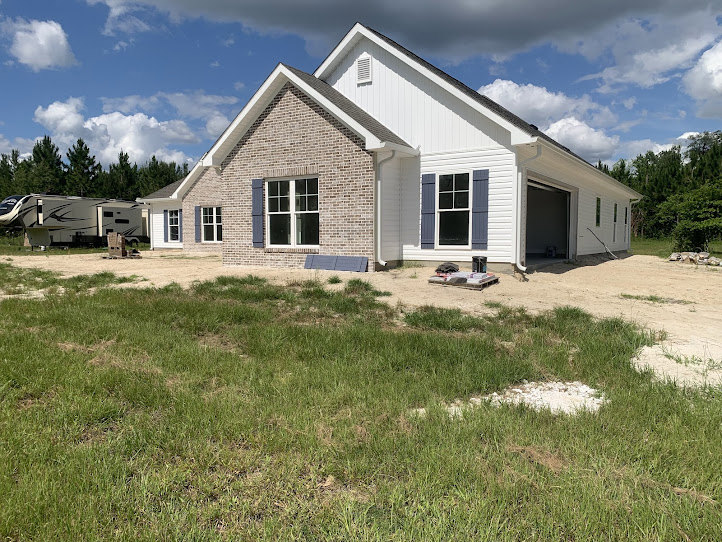 Two-story home with attached garage, gray siding, white trim, large windows, manicured grass lawn, mature trees, and partly cloudy sky
