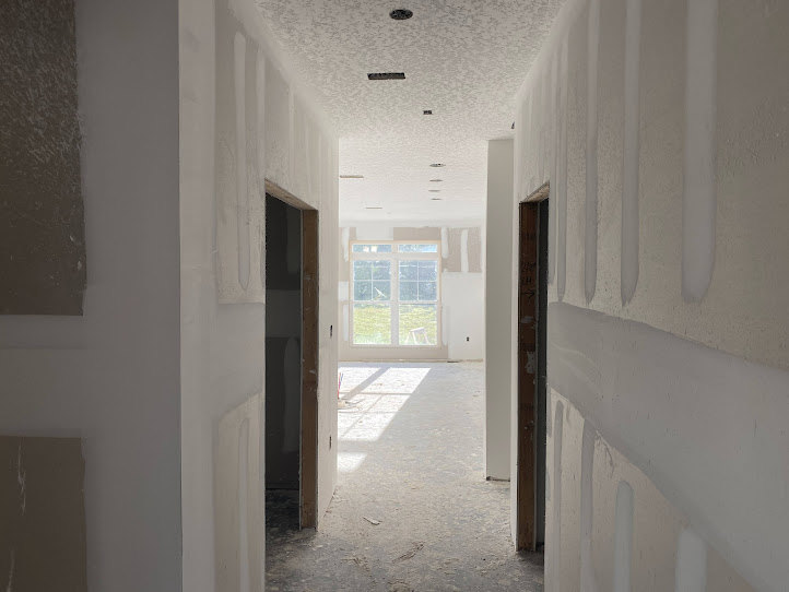 Hallway with smooth white plaster walls, large window allowing daylight, light wood flooring, and simple crown molding