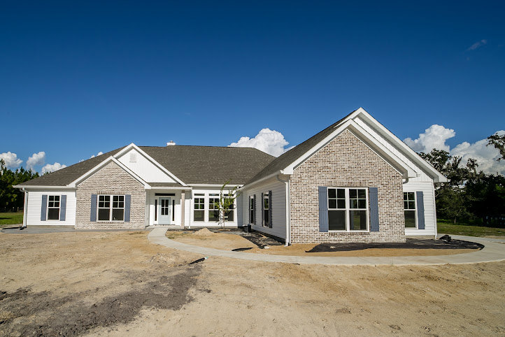 Partially built house with exposed framing, dirt driveway leading to the porch, cloudy sky overhead, Robert Frost Farm visible in the background