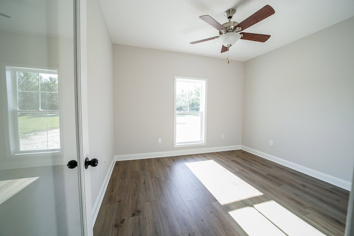 Ceiling fan with light fixture mounted on smooth gray ceiling above wood laminate flooring in a neutral-toned room with plaster walls