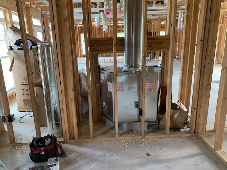 Exposed wood framing with silver metal chimney vent, construction tools and materials scattered on unfinished floor, visible beams and insulation