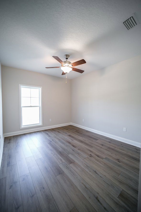 Ceiling fan with light fixture mounted on white plaster ceiling above hardwood floor in a spacious room with neutral walls