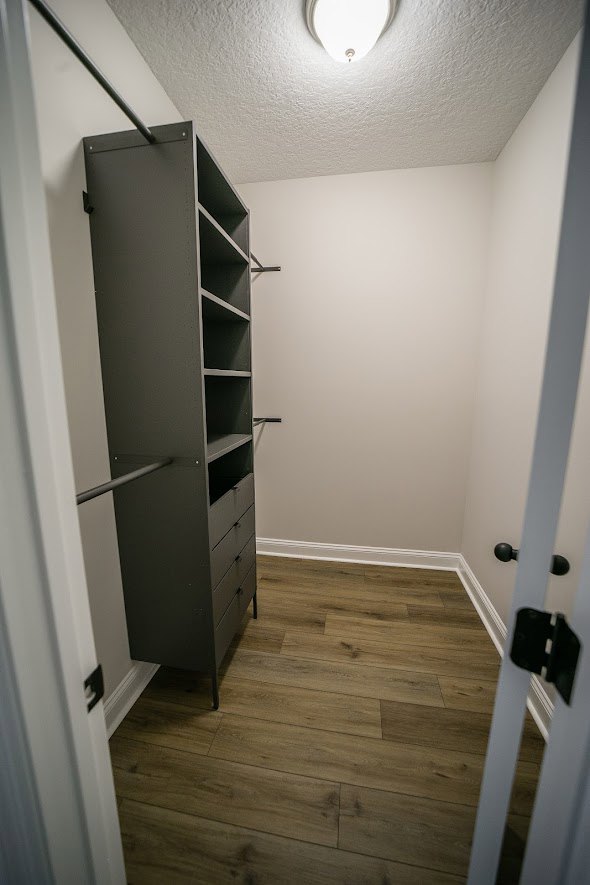 Walk-in closet with built-in shelves, hanging bar, light wood flooring, white plaster walls, and cabinetry.