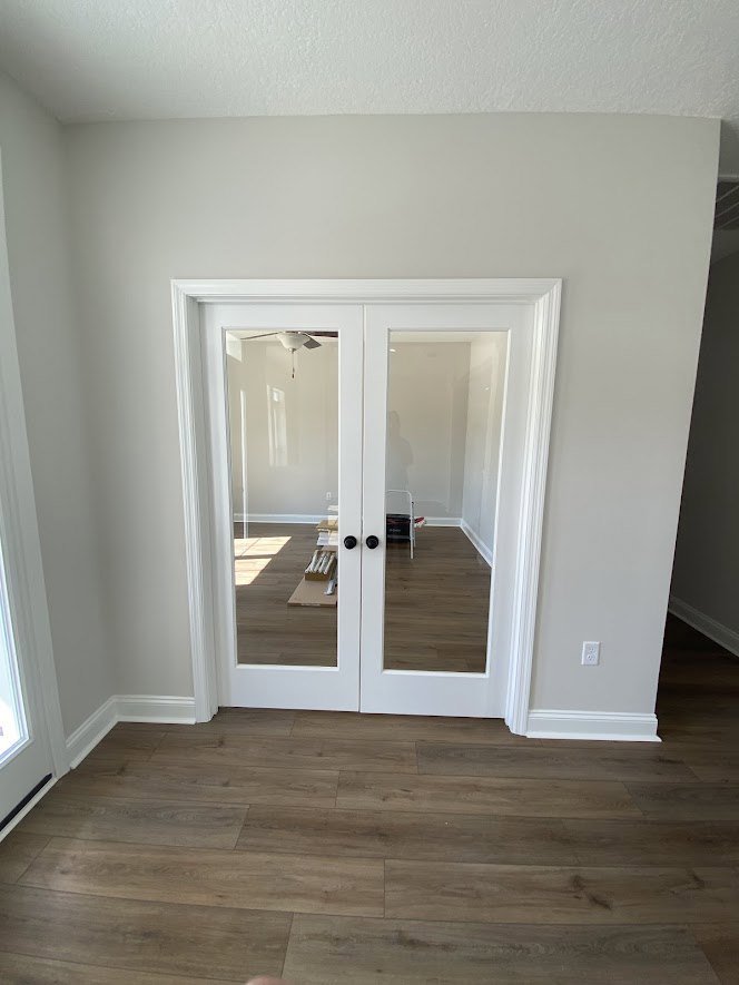White double glass doors with white trim, wood flooring, white walls, and a ceiling light fixture in a residential room