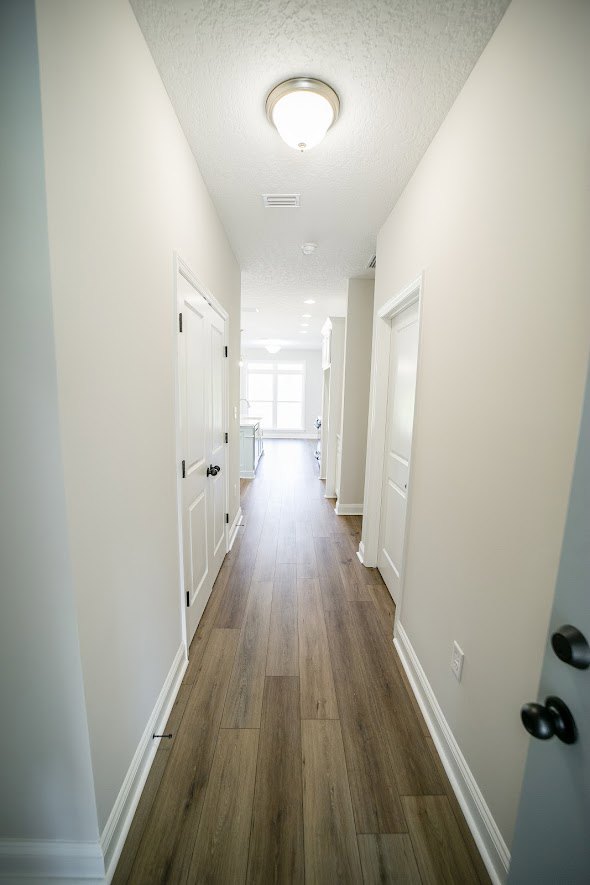 Hallway featuring white plaster walls, hardwood flooring, and doorways leading to adjacent rooms