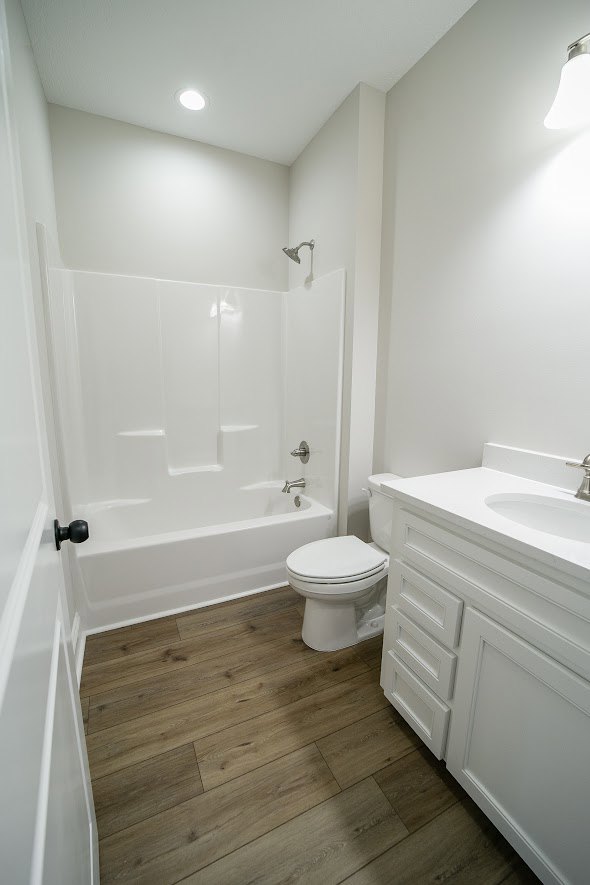 White bathroom featuring a pedestal sink, modern toilet with white lid, and tiled floor; partial view of a white bathtub along the wall.
