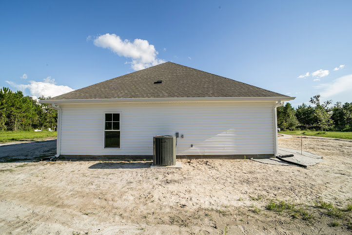 Modern home exterior featuring attached garage, prominent black rectangular structure, light siding, manicured lawn, mature trees, and partly cloudy sky.