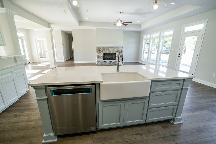 Modern kitchen featuring white cabinetry, silver dishwasher with blue trim, white sink with silver faucet, stainless steel stove, light stone countertops, and wood flooring.