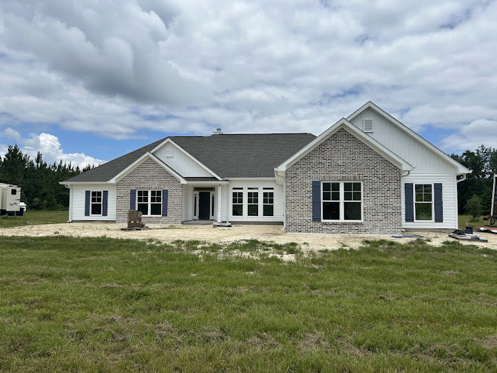 Brick and white exterior home with large grassy yard, blue accent wall around window, covered porch, and partly cloudy sky