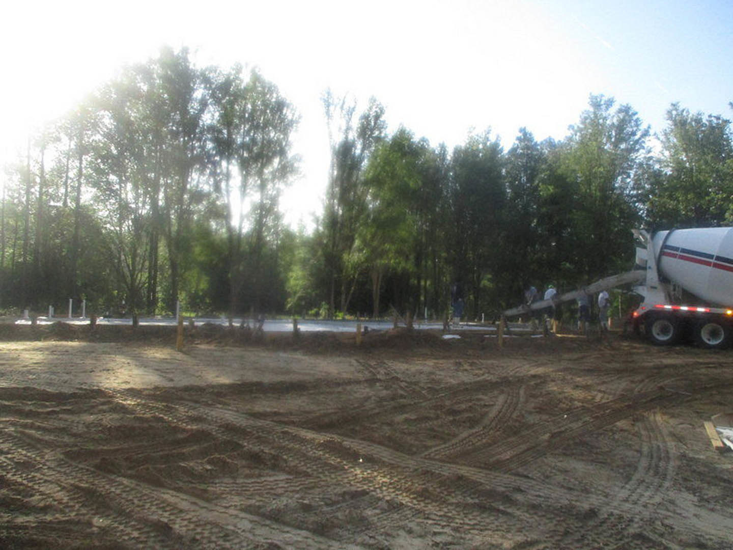 Dirt field with deep tire tracks, scattered soil, and distant trees under an open sky