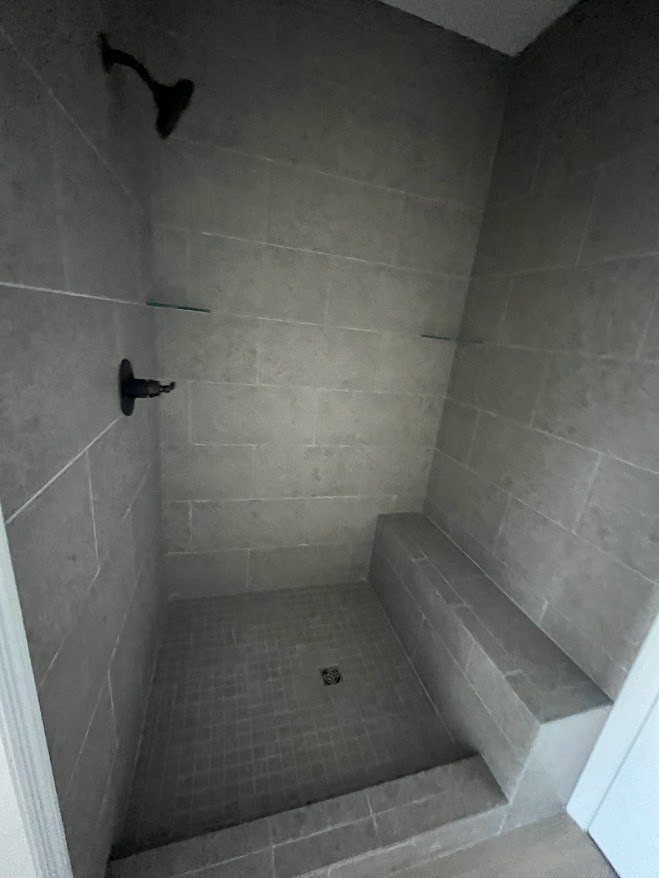 Walk-in shower with built-in bench, light plaster walls, glass enclosure, and tiled floor adjacent to bathroom fixtures.