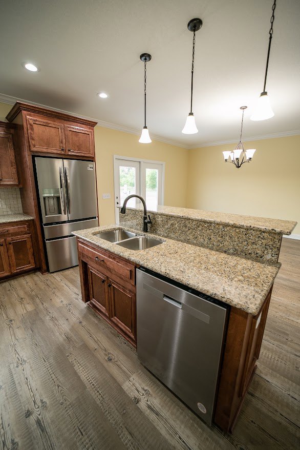 Granite countertop kitchen with stainless steel sink, tile backsplash, wood cabinetry, stainless steel refrigerator and dishwasher