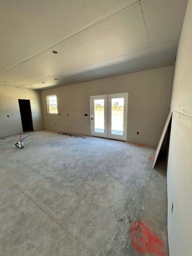 Spacious room with red accent wall, double glass-panel doors, multiple windows, light-colored plaster ceiling, composite flooring, and a door featuring a small sign.