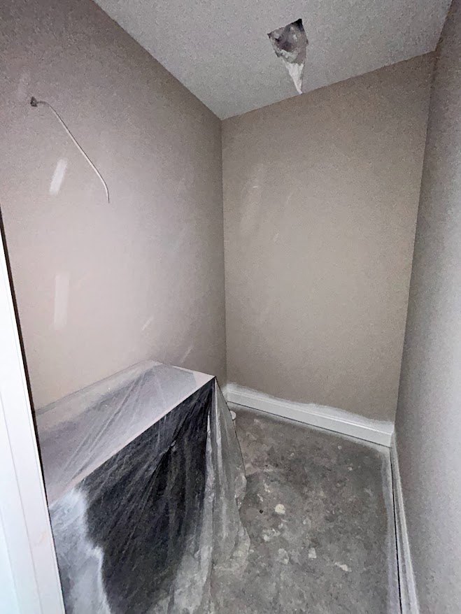 Bathroom with grey floor and white trim, plaster walls, plastic wrap covering a corner, partial view of ceiling.