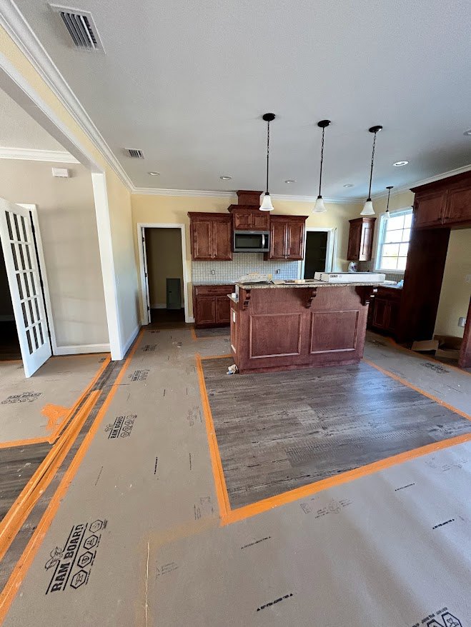 Open kitchen with marble-topped bar, wood flooring with yellow tape, white cabinetry, pendant lights, and a door leading to another room.