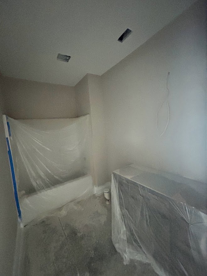 Bathroom with a freestanding bathtub wrapped in protective plastic, light plaster walls, and smooth ceiling.