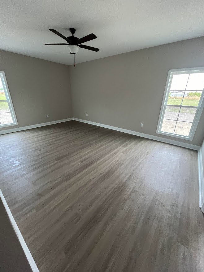 Bright room with wood flooring, ceiling fan with light, large windows overlooking green field