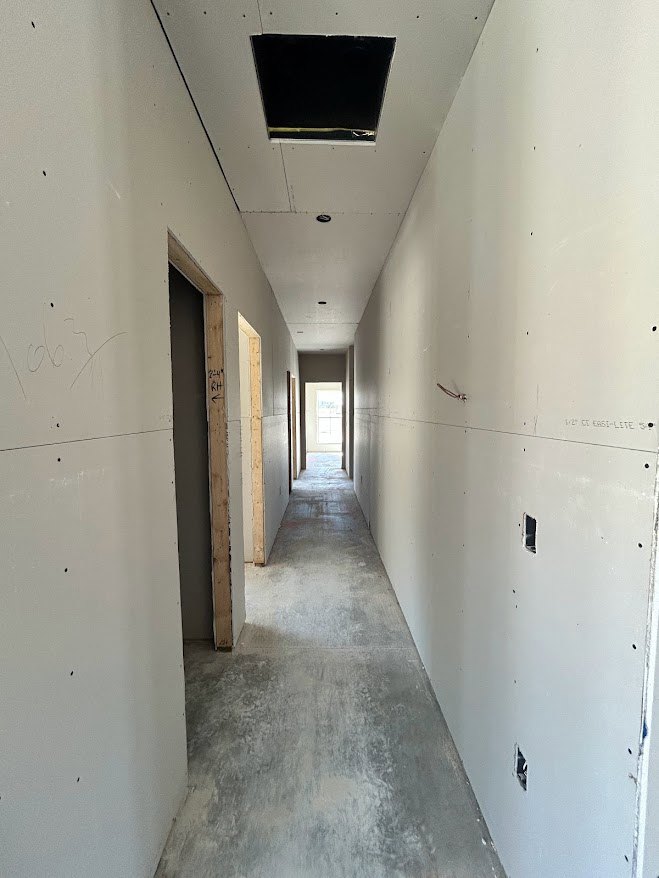 Hallway with smooth white plaster walls, light concrete flooring, square window with black trim, wood-framed door featuring glass inset