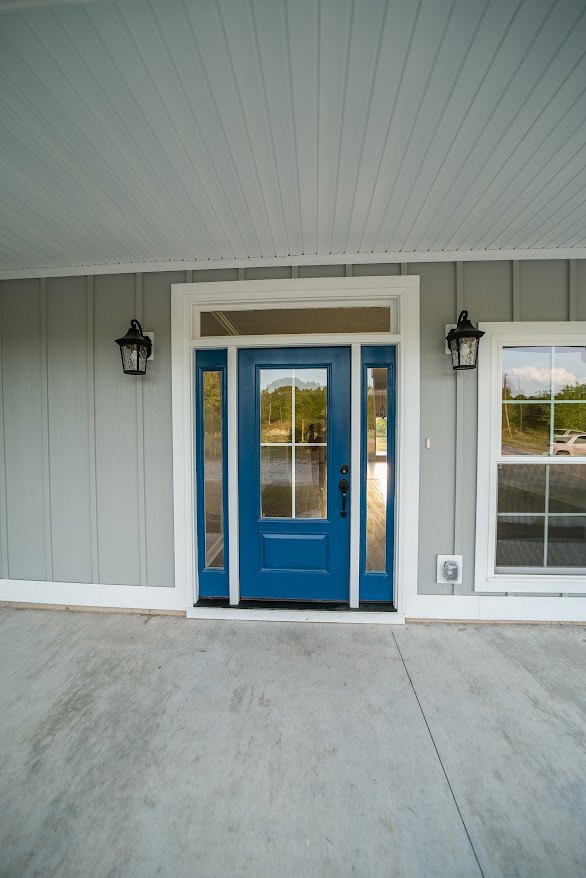 Blue door with glass panes, concrete floor, windows showing car and person reflection, white ceiling with vertical lines