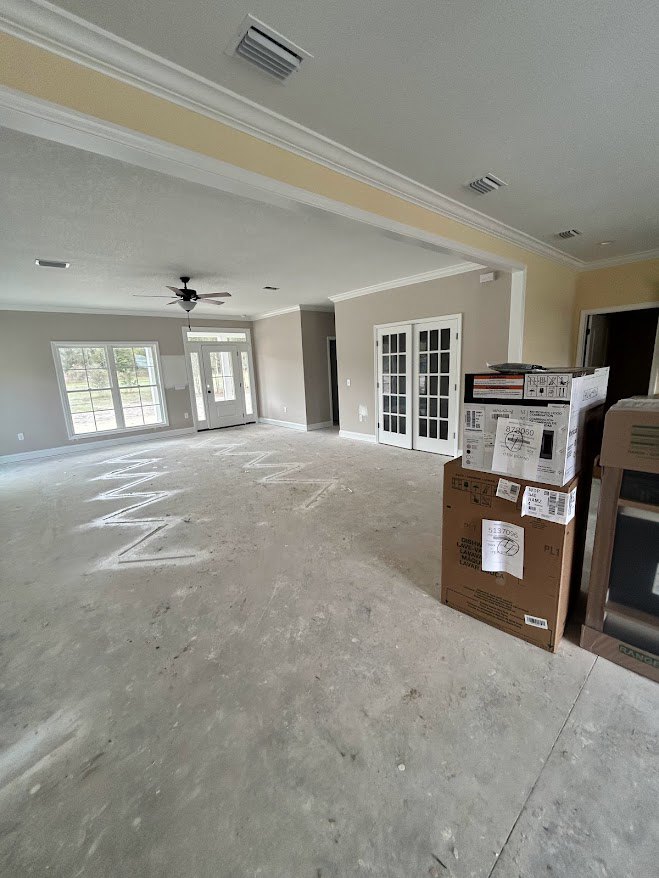 Unfinished room with stacked cardboard boxes, white double doors with glass panes, multi-pane window, ceiling fan, visible wooden framing, and labeled paper with numbers.