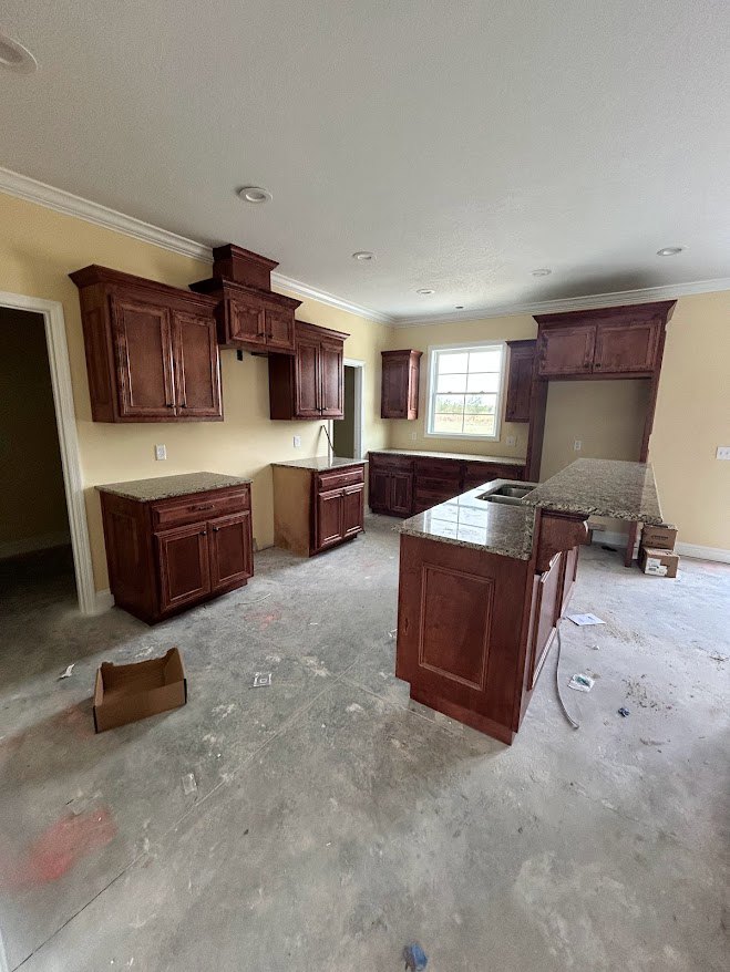 Marble countertop with wooden cabinets, white-framed window, brown storage box on counter, plaster walls, light wood flooring, recessed ceiling lighting