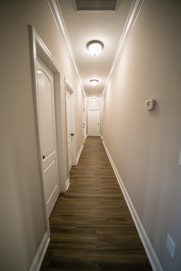 Long hallway with white doors, white walls, white trim, and wood flooring