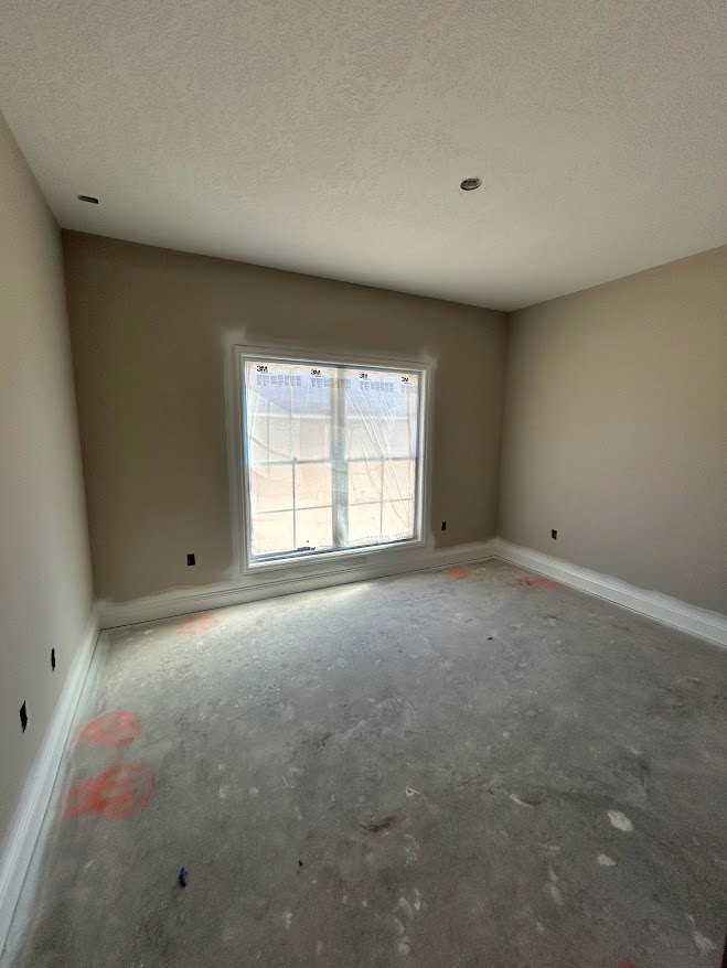 Room with large window, concrete floor, white plaster walls, and ceiling with visible spot; window partially covered with plastic sheeting.