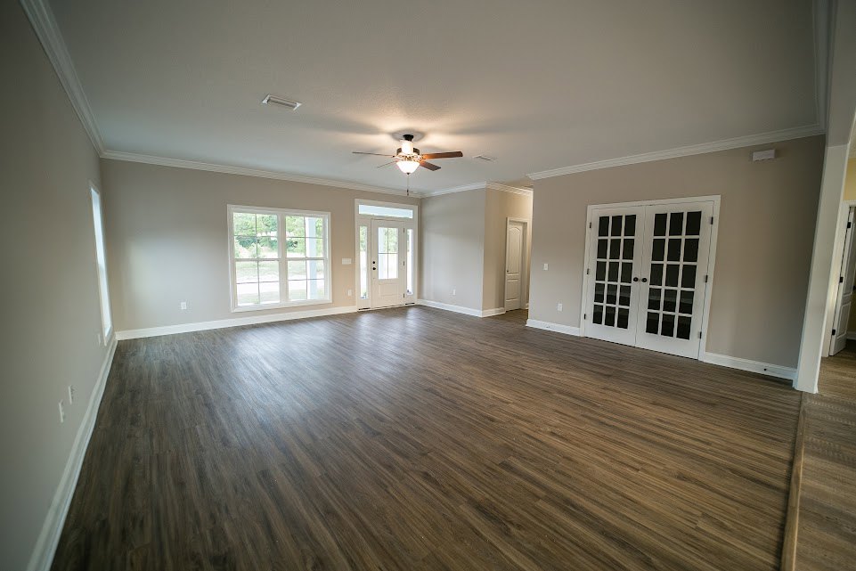 Spacious room with hardwood flooring, white double doors featuring black glass panels, ceiling fan with light, and window overlooking trees