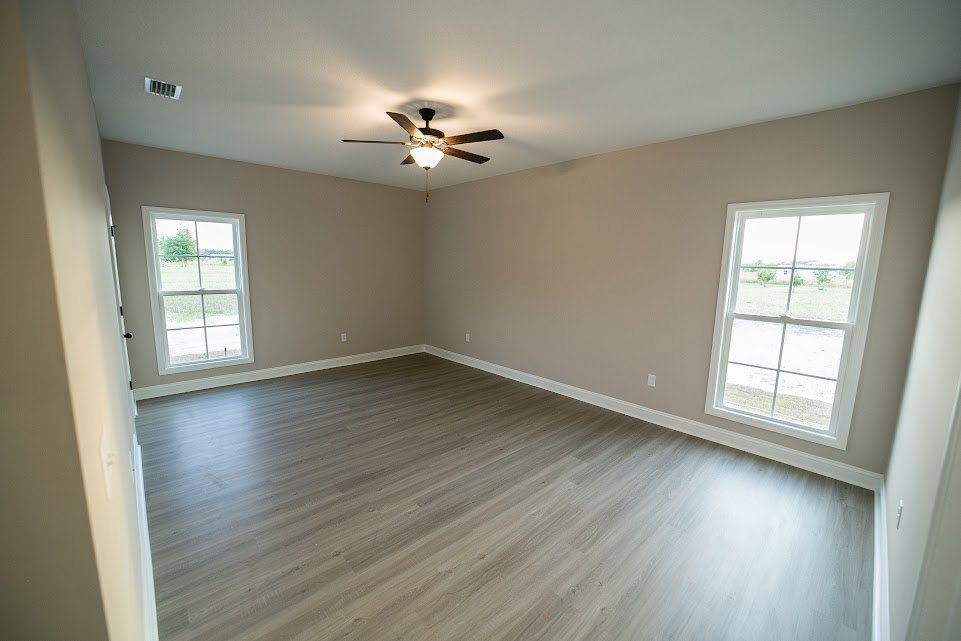 Ceiling fan with light fixture, large windows overlooking grassy field, wood laminate flooring, white plaster walls