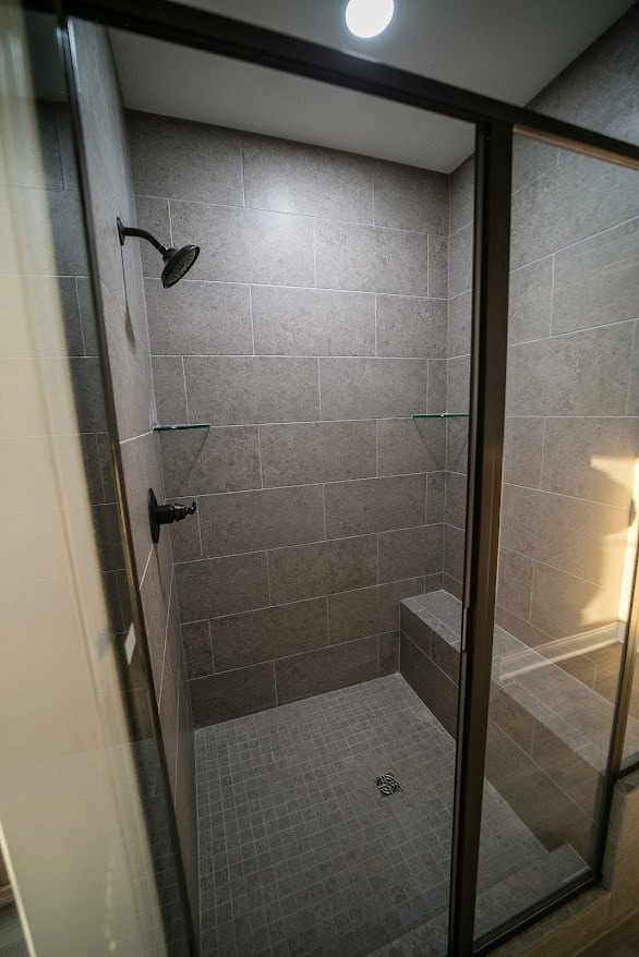 Walk-in shower with frameless glass door, tiled walls, chrome shower head, and built-in niche