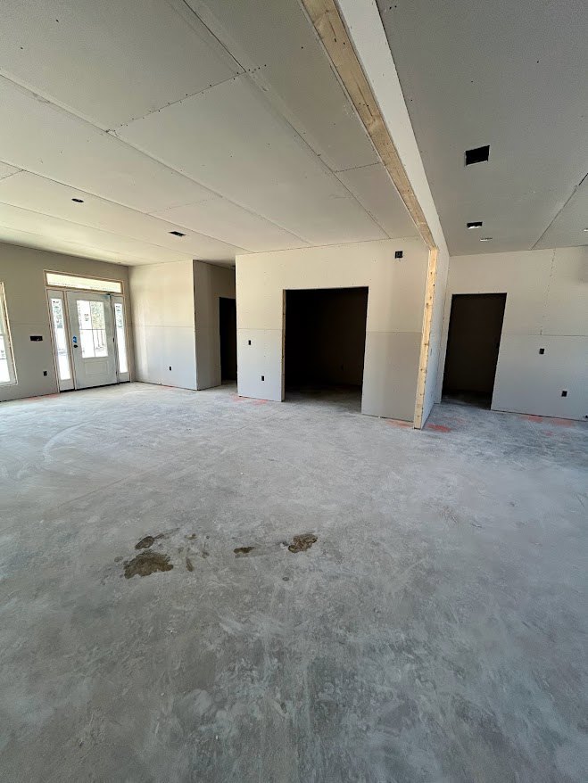 Concrete floor room with white framed glass door, open black door, white walls, ceiling, and scattered moving boxes