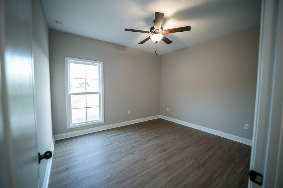 Ceiling fan with light fixture, white-framed window, wood flooring, neutral walls