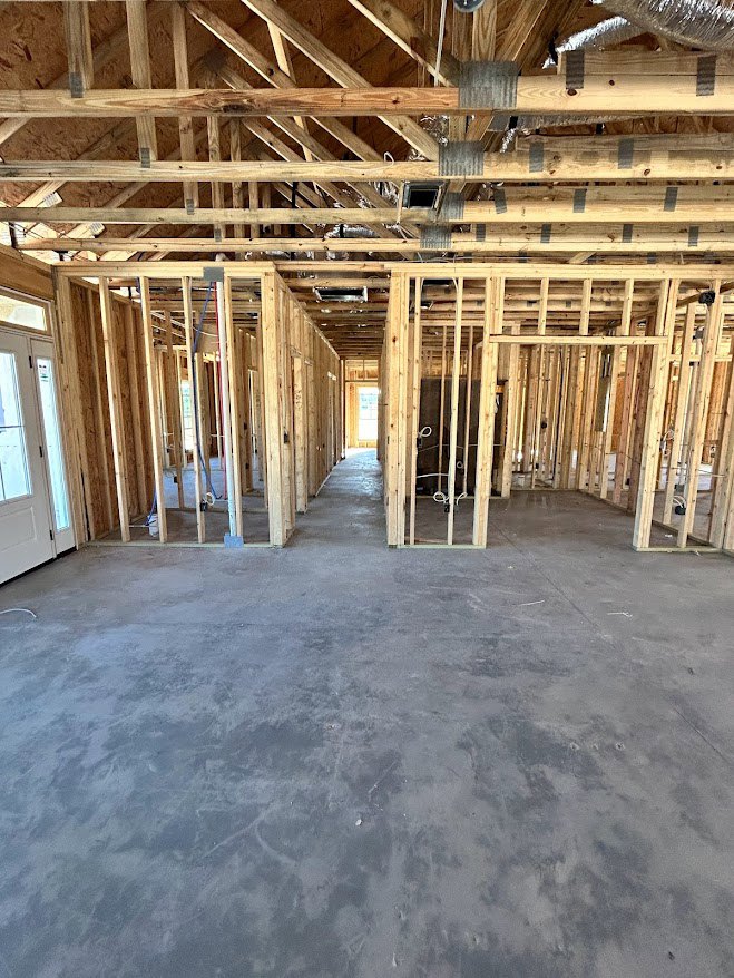 Exposed wood ceiling beams, concrete floor with visible cracks, unfinished wooden framing, and a closed door with metal hinge