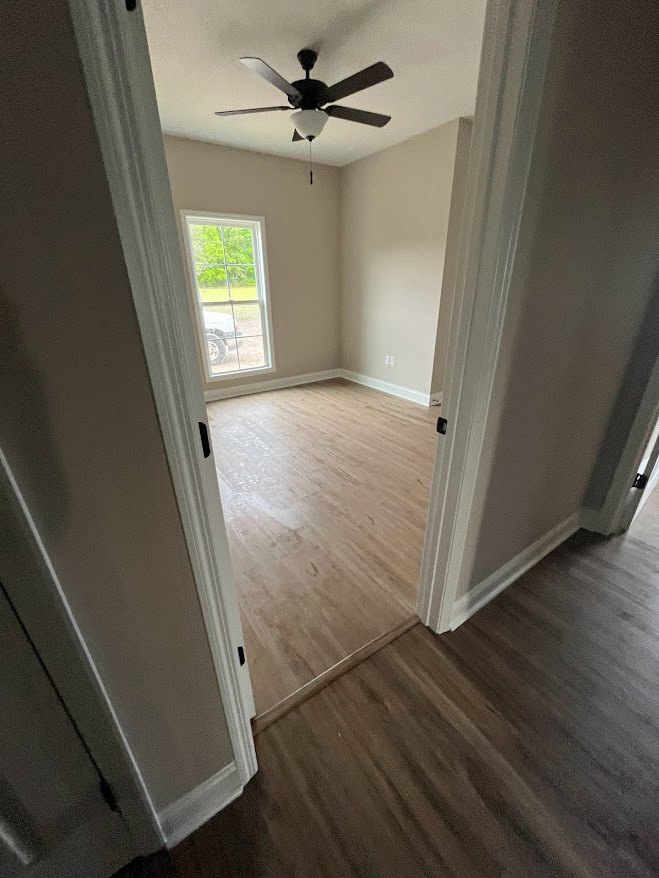 Ceiling fan mounted on white plaster ceiling above hardwood floor, neutral walls, and baseboard trim in residential interior room