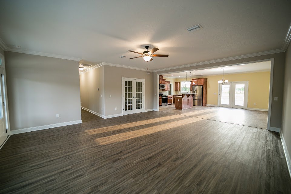 Spacious open floor plan featuring hardwood flooring, white double doors with glass panes, and a ceiling fan with light fixture.
