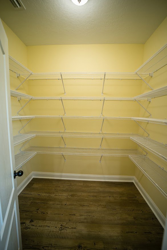 Empty closet with white shelving, wood floor, white baseboard, and yellow accent wall