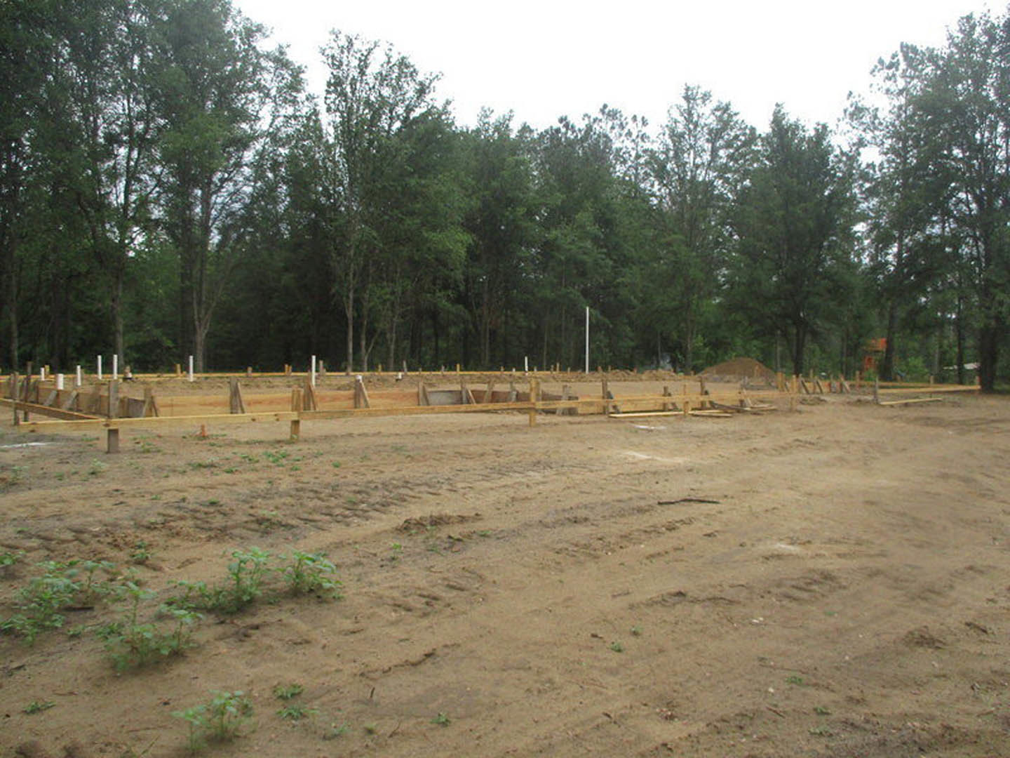Dirt construction site with tire tracks, bordered by dense trees under a clear sky