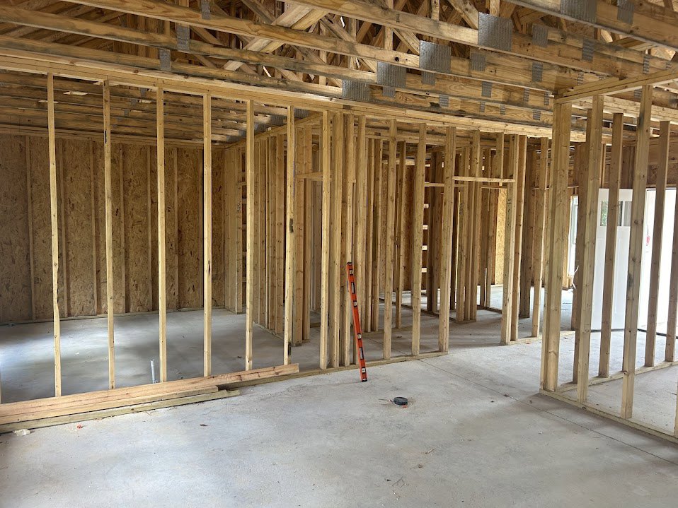 Exposed wood framing and beams inside a house under construction, with construction tools and insulation visible on unfinished floors and ceiling.