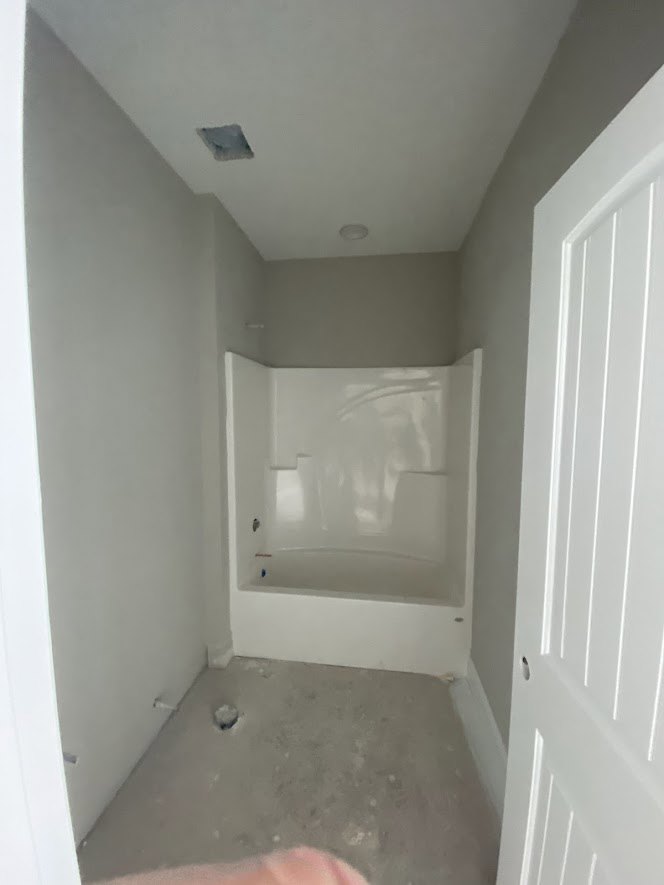 White freestanding bathtub beside a white paneled door in a bathroom with smooth plaster walls and neutral finishes