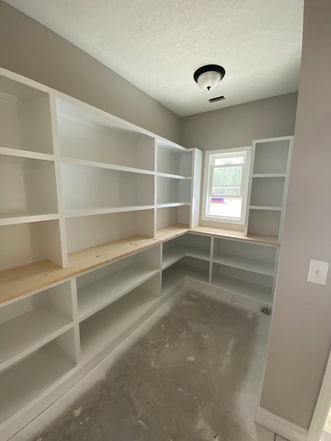 Concrete floor and white built-in shelves beneath a large window with a white frame, plaster walls, ceiling, and a light switch visible on the wall.