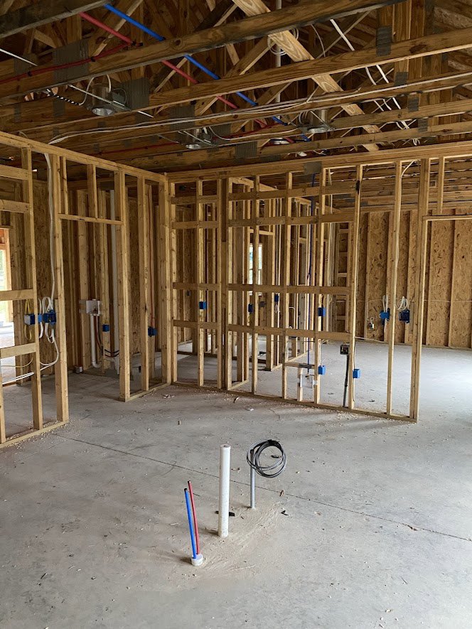 Unfinished room with exposed wood framing, ceiling beams, electrical wiring, and plumbing pipes set in a concrete floor
