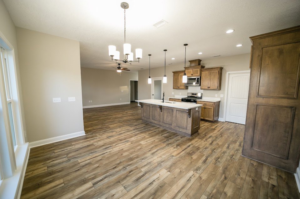 Open kitchen and dining area with hardwood floors, white cabinetry, central kitchen island, and modern chandelier above dining table