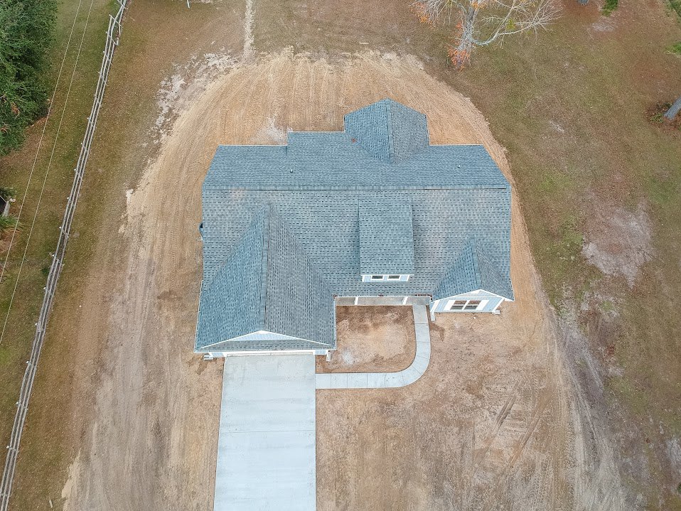 Modern two-story home with light siding, paved driveway, green lawn, leafless tree, wooden fence, and white utility box on dirt area