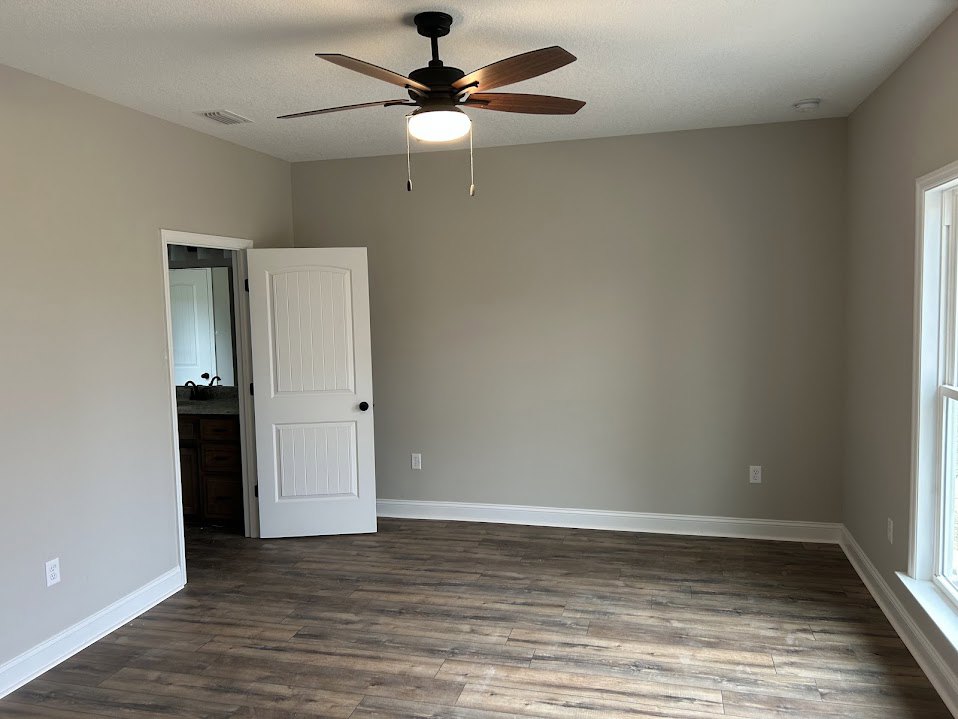 Ceiling fan with light fixture, wood flooring with white trim, white door with black knob, window with white frame, neutral walls
