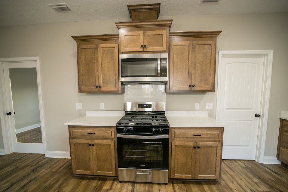 Kitchen with natural wood cabinets, black stove and grill, open microwave door, white door with black handle, light countertops, and neutral walls