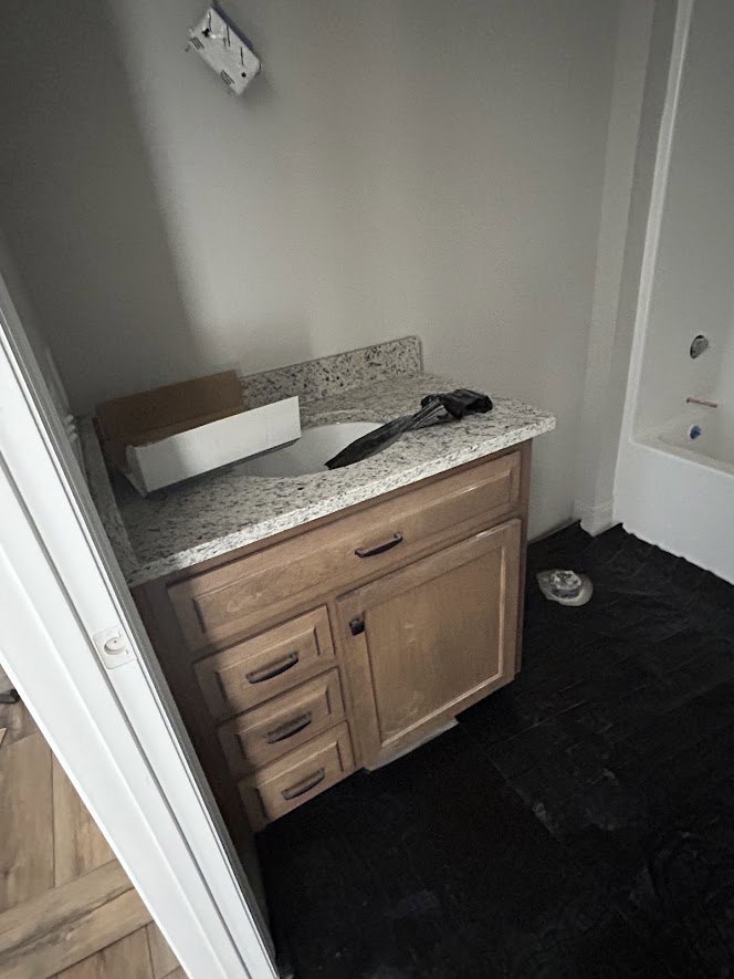 Bathroom featuring a freestanding tub, marble countertop with black faucet, white cabinetry, tiled floor, and white door with matching knob